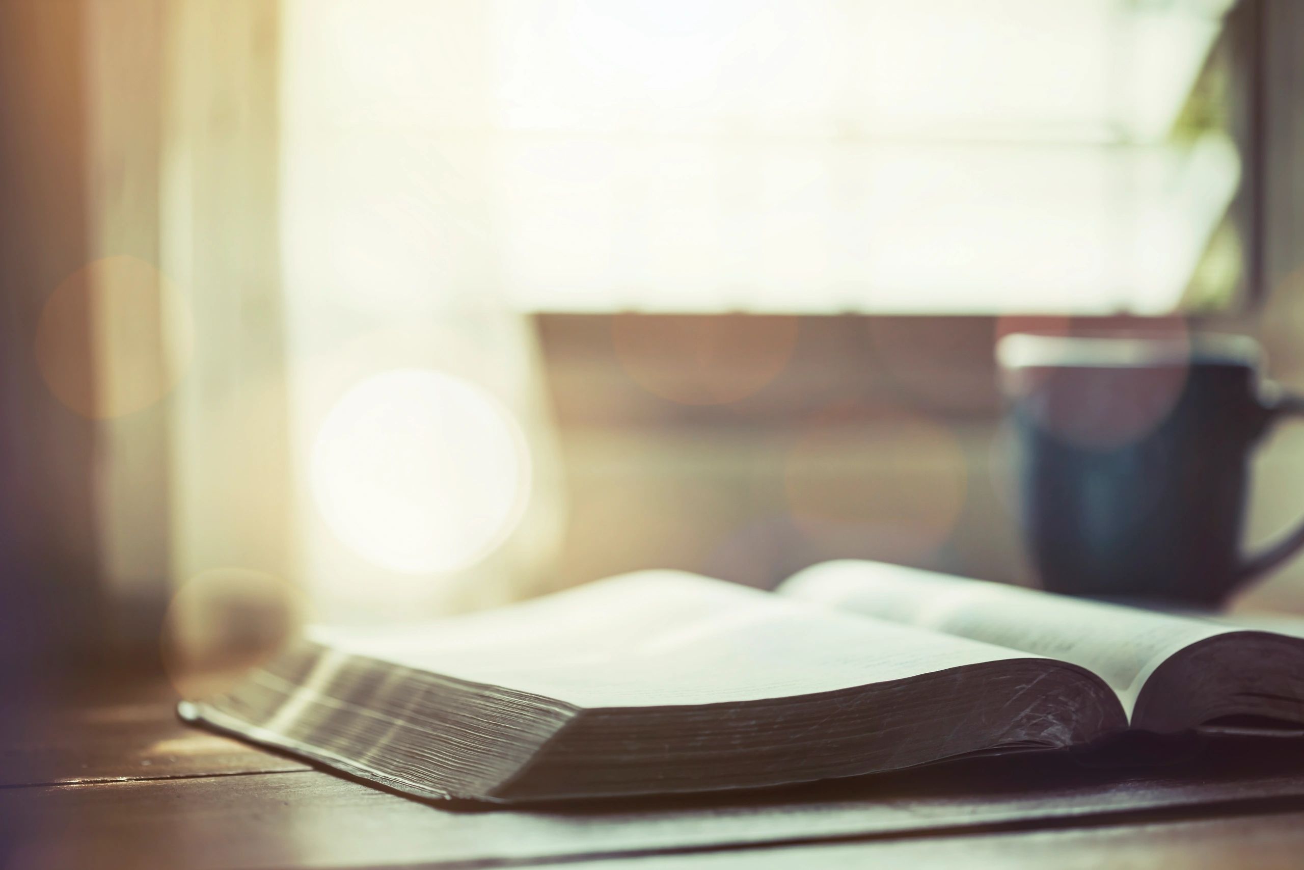 Open Bible with coffee on a wooden table near a window