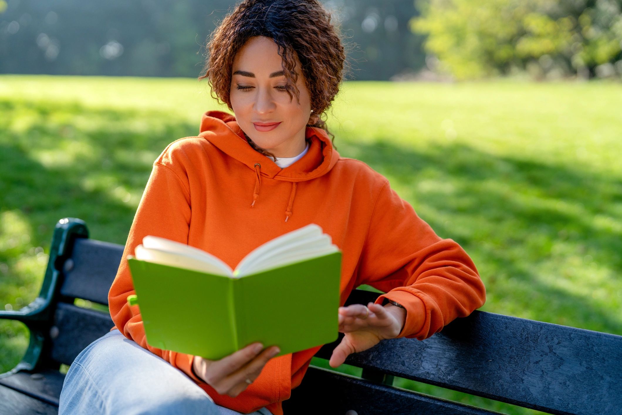 Woman reading a book on a bench in a sunny park